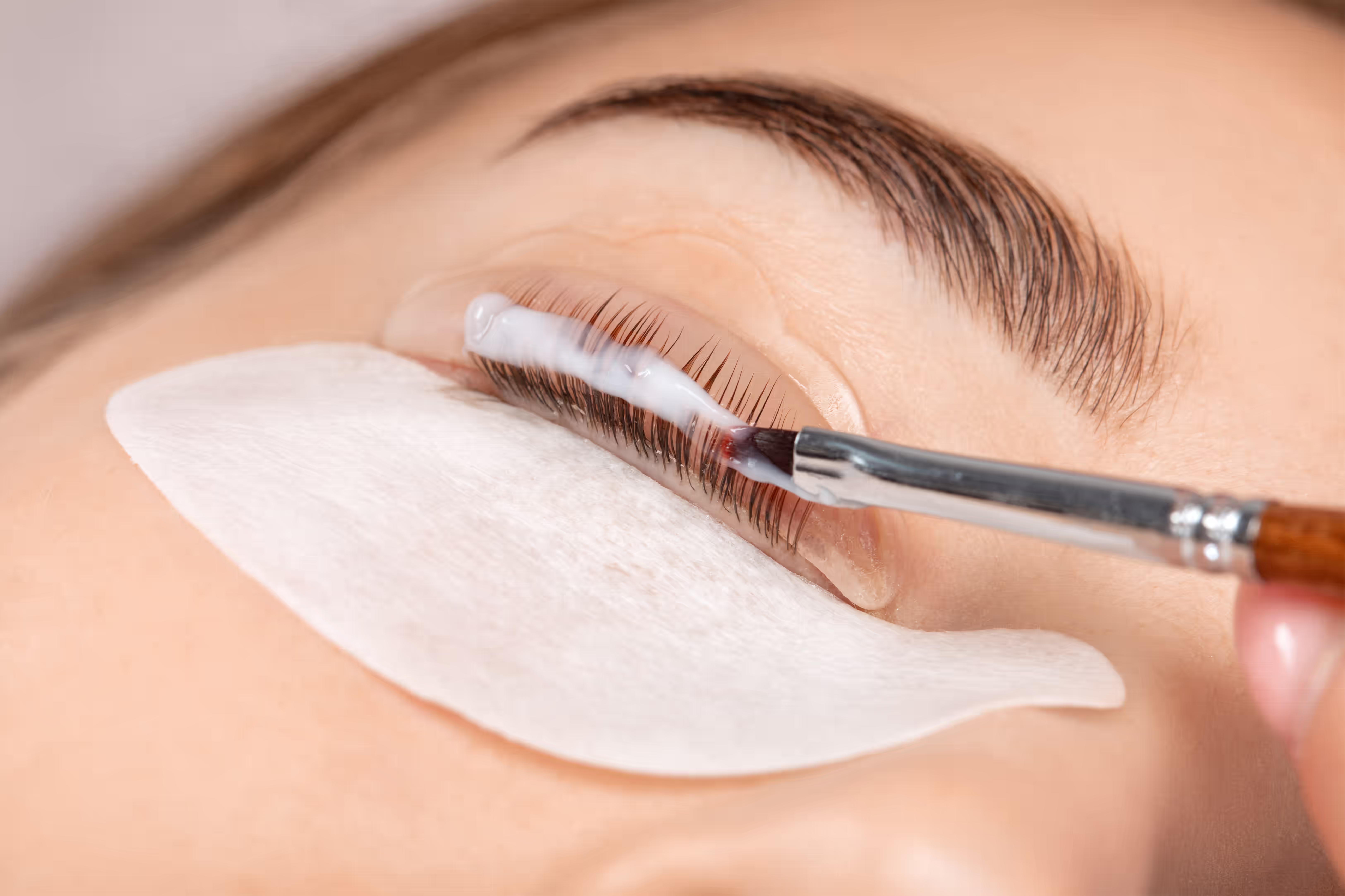 Close-up of a beautician applying lifting solution to eyelashes with a brush during a professional lash lift treatment.