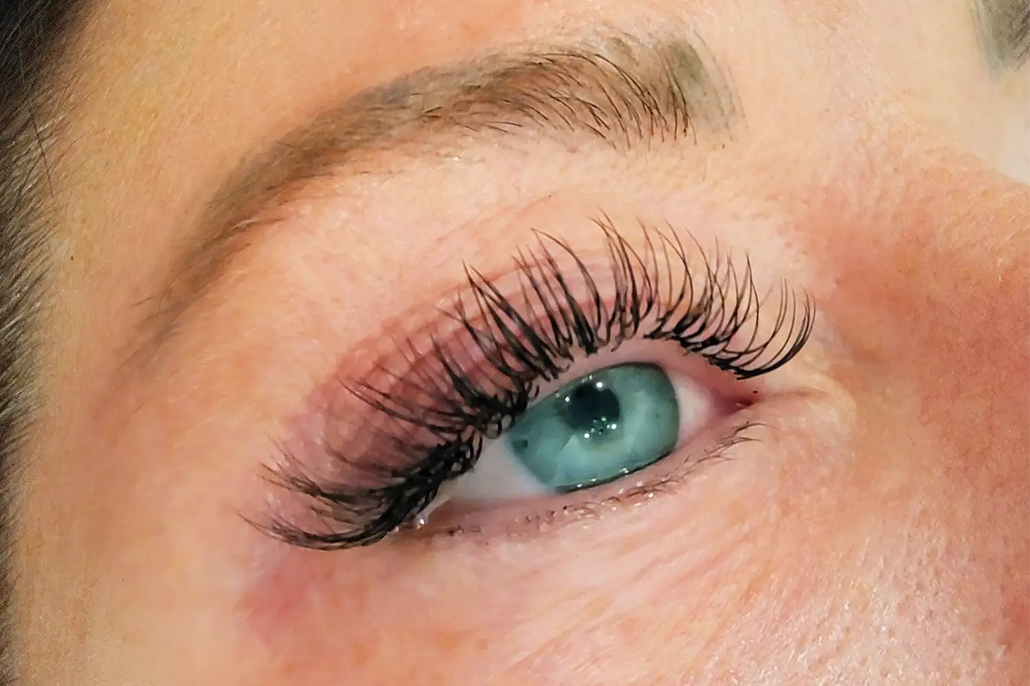 Close up of eye after lash service showing longer lifted lashes with enhanced curl, darker definition, and fuller lash line