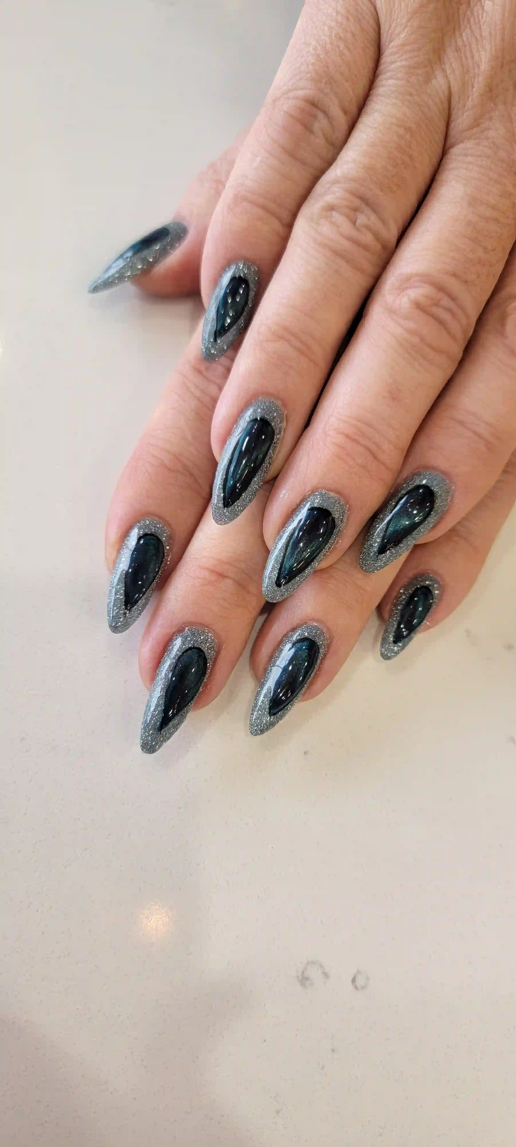 Dark chrome almond nails with silver glitter outline and high shine finish, modern gel manicure by Opalya mobile spa in Toronto