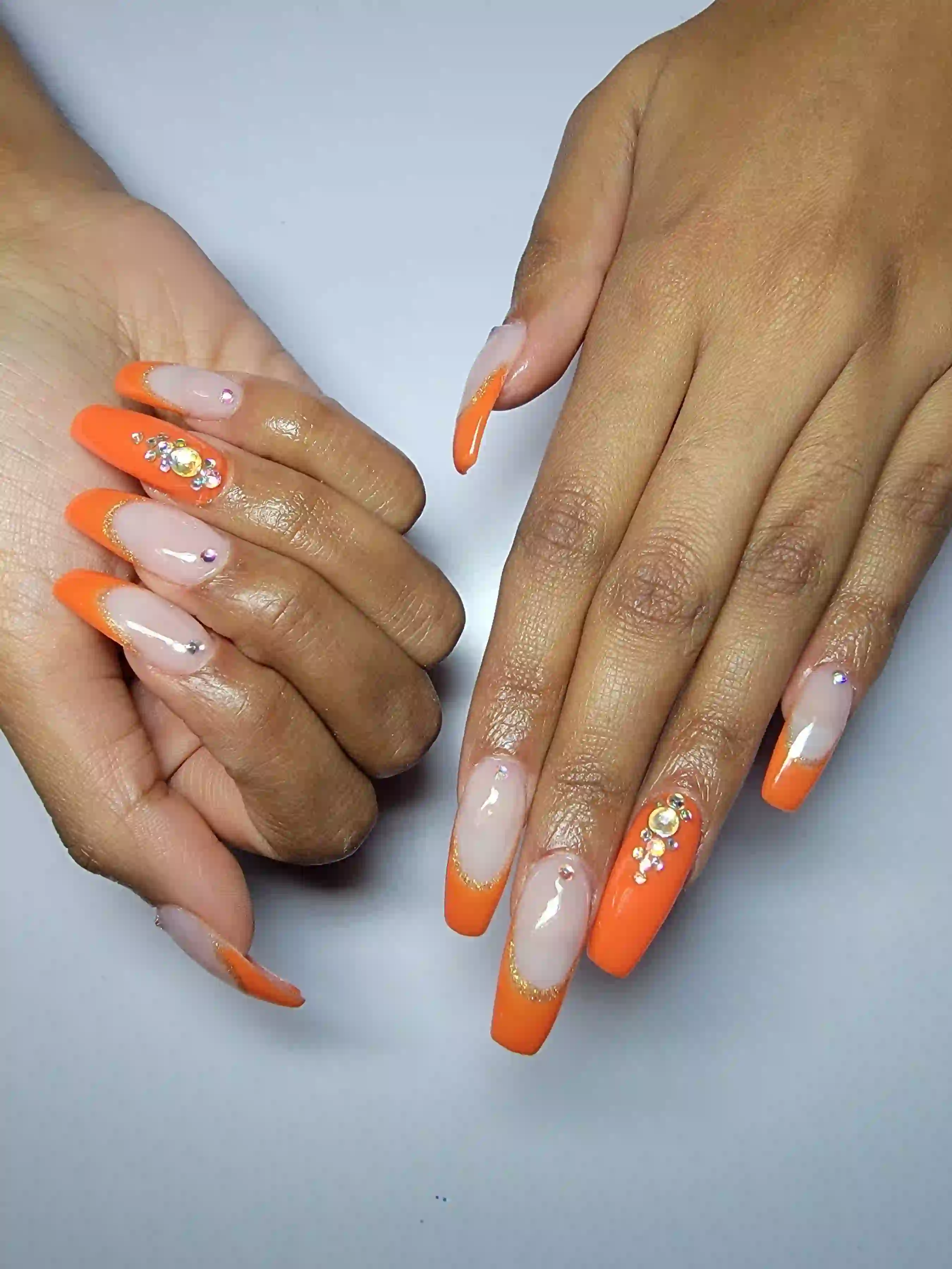 Bright orange coffin nails with rhinestone accents and glossy nude base, bold acrylic nail design by Opalya mobile nail service