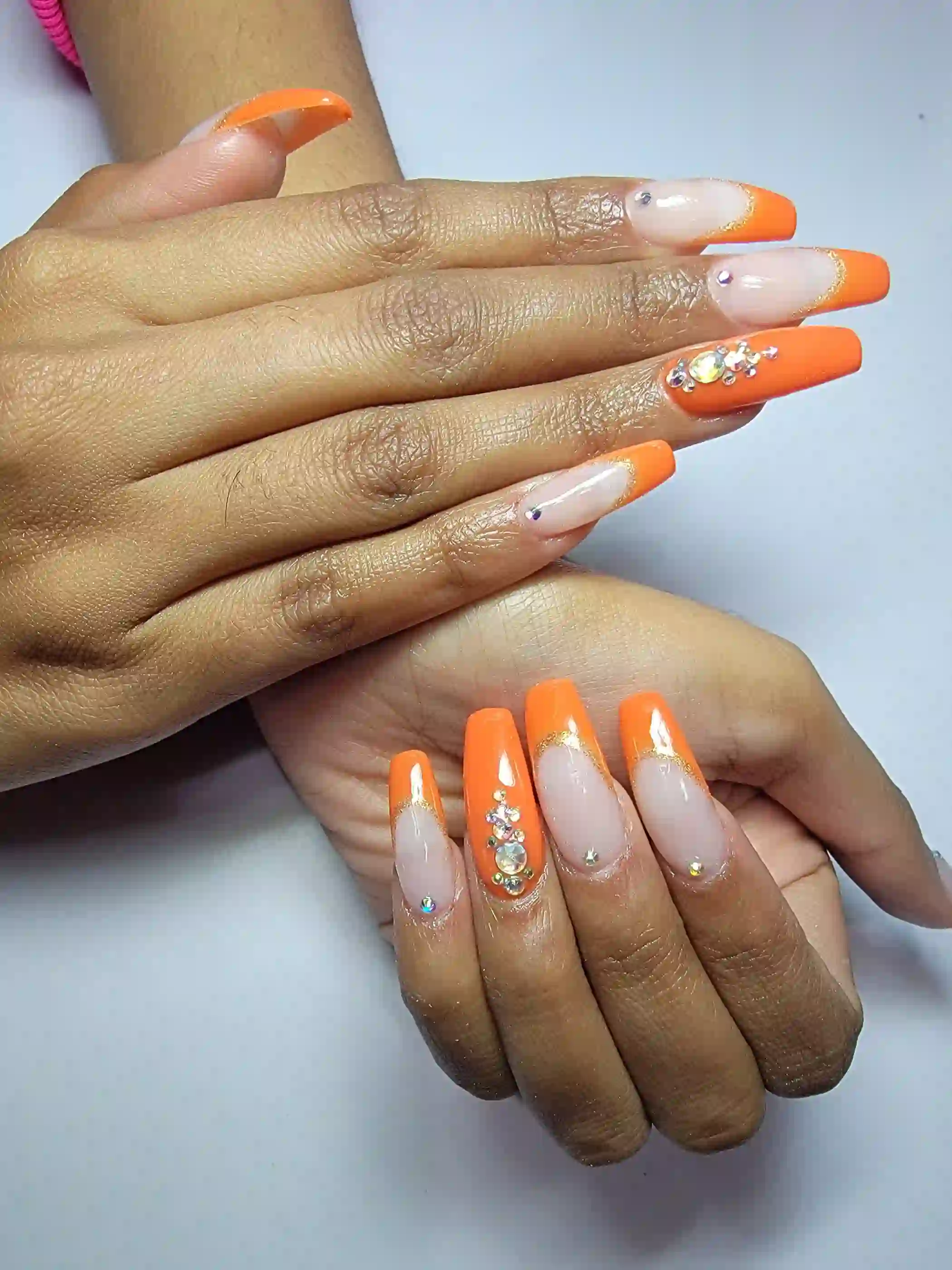 Bright orange coffin nails with rhinestone accents and glossy nude base, statement acrylic nails by Opalya mobile nail technician