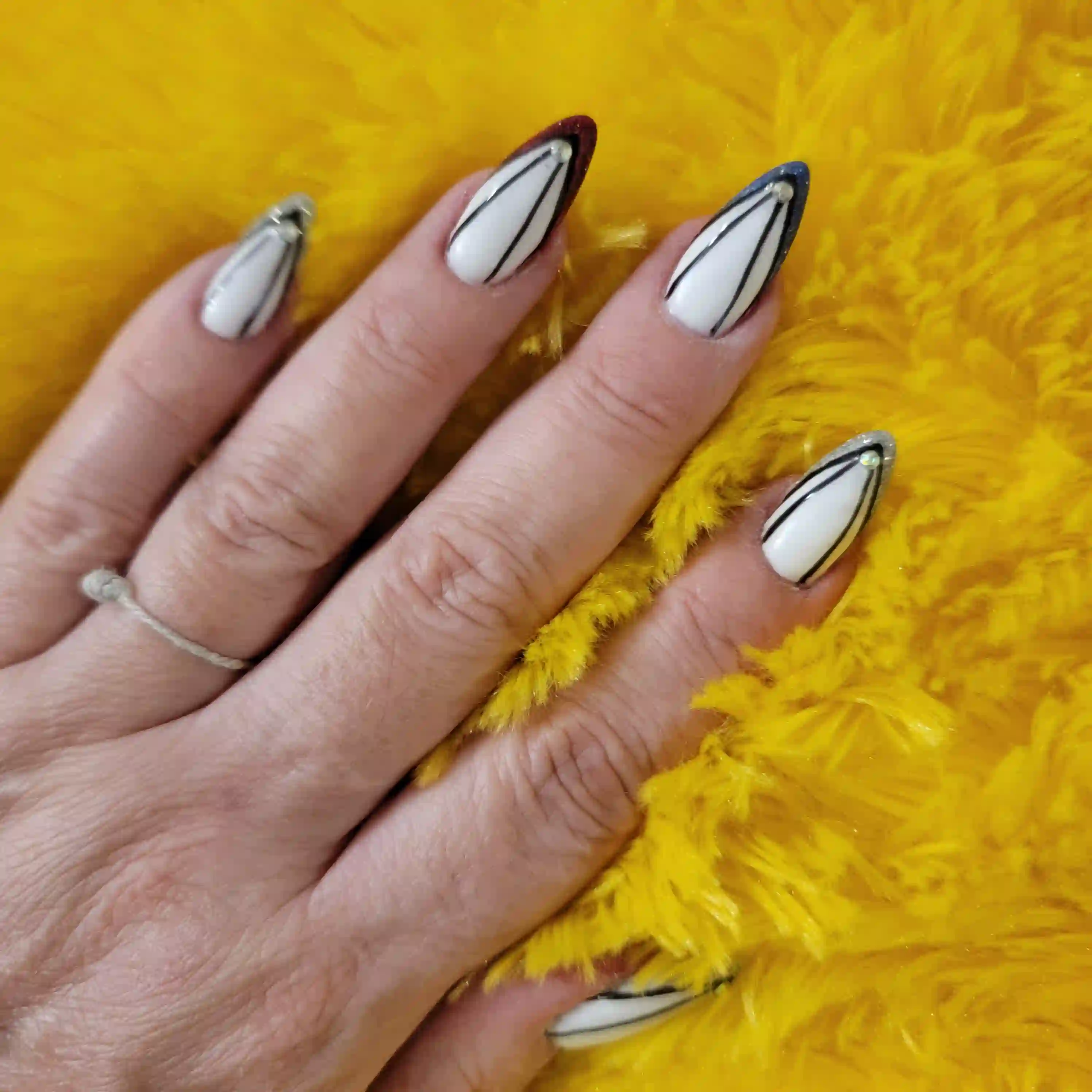 White almond nails with black line art and chrome outlined tips on yellow textured background, modern minimalist nail design by Opalya