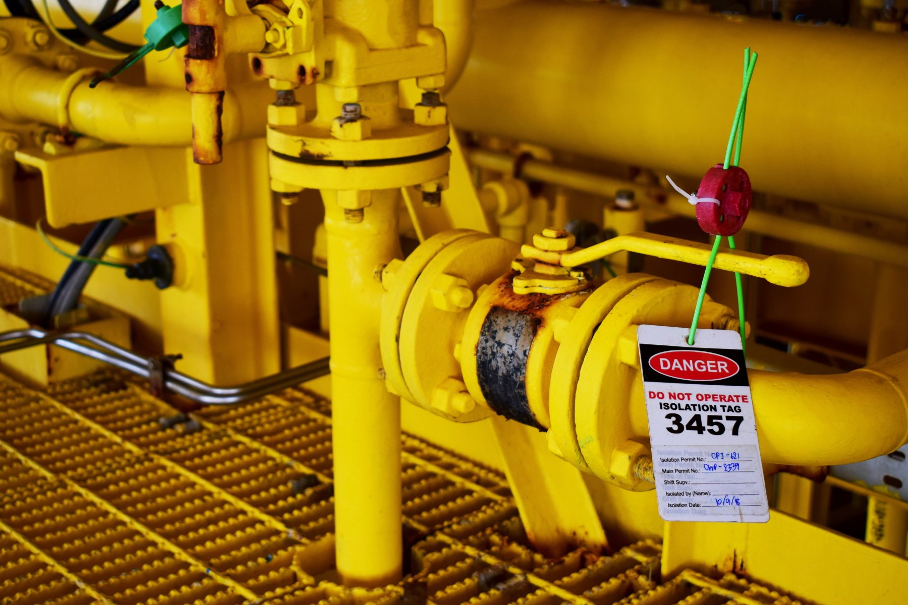 Yellow industrial valve with a red and white lockout tag reading 'DANGER DO NOT OPERATE ISOLATION TAG 3457' attached by green ties.