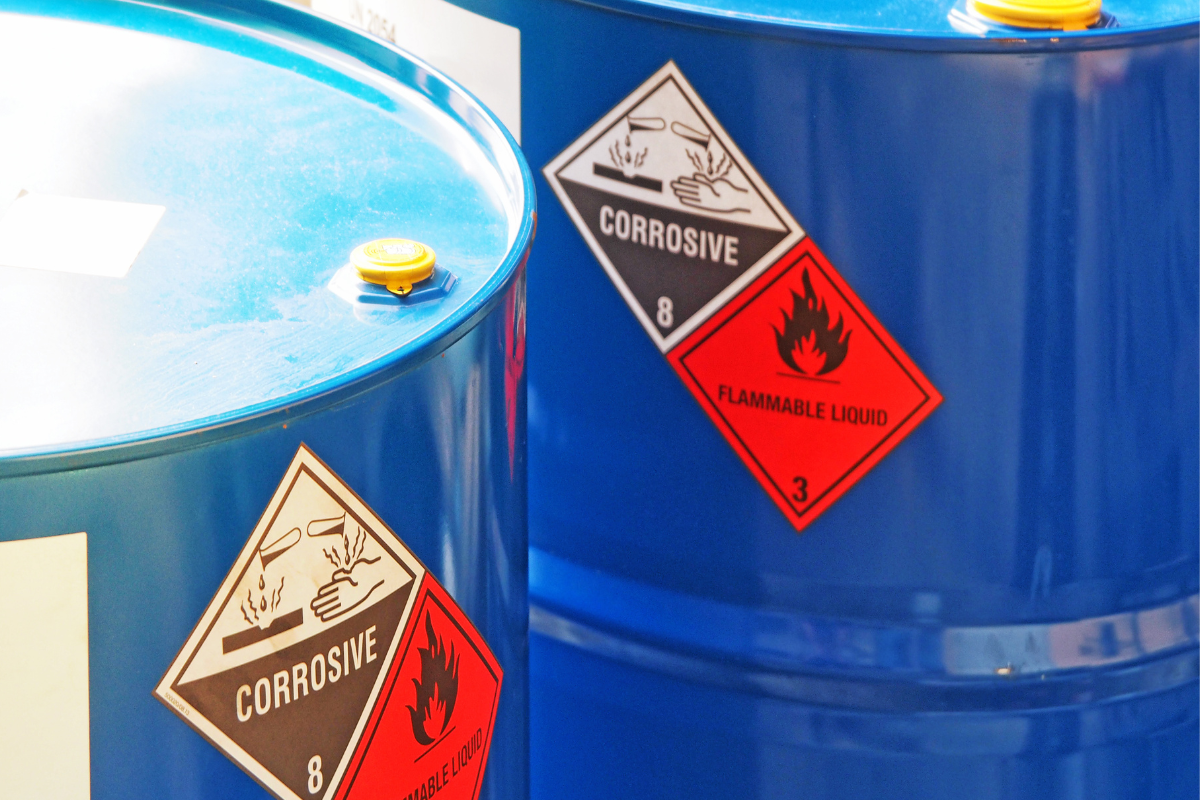 Blue barrels labeled with corrosive and flammable liquid hazard signs.