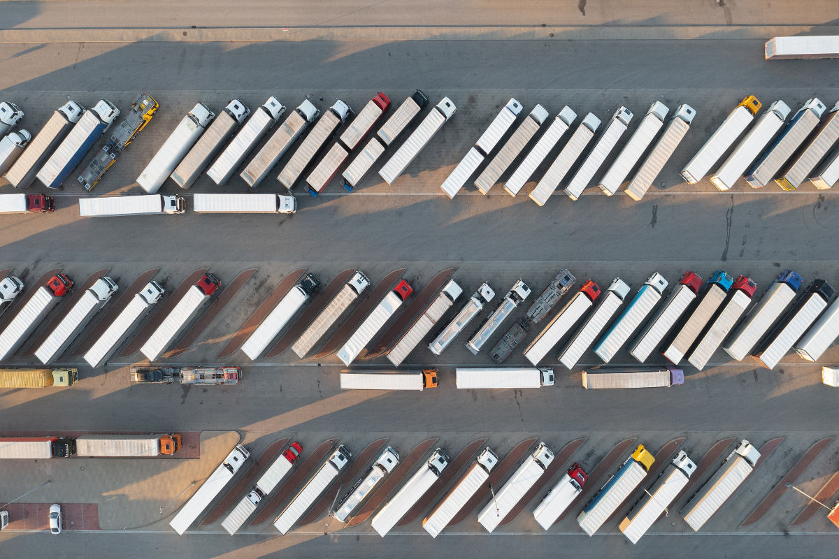 Aerial view of a large parking lot filled with rows of parked white semi-trailer trucks and a few colored trucks.