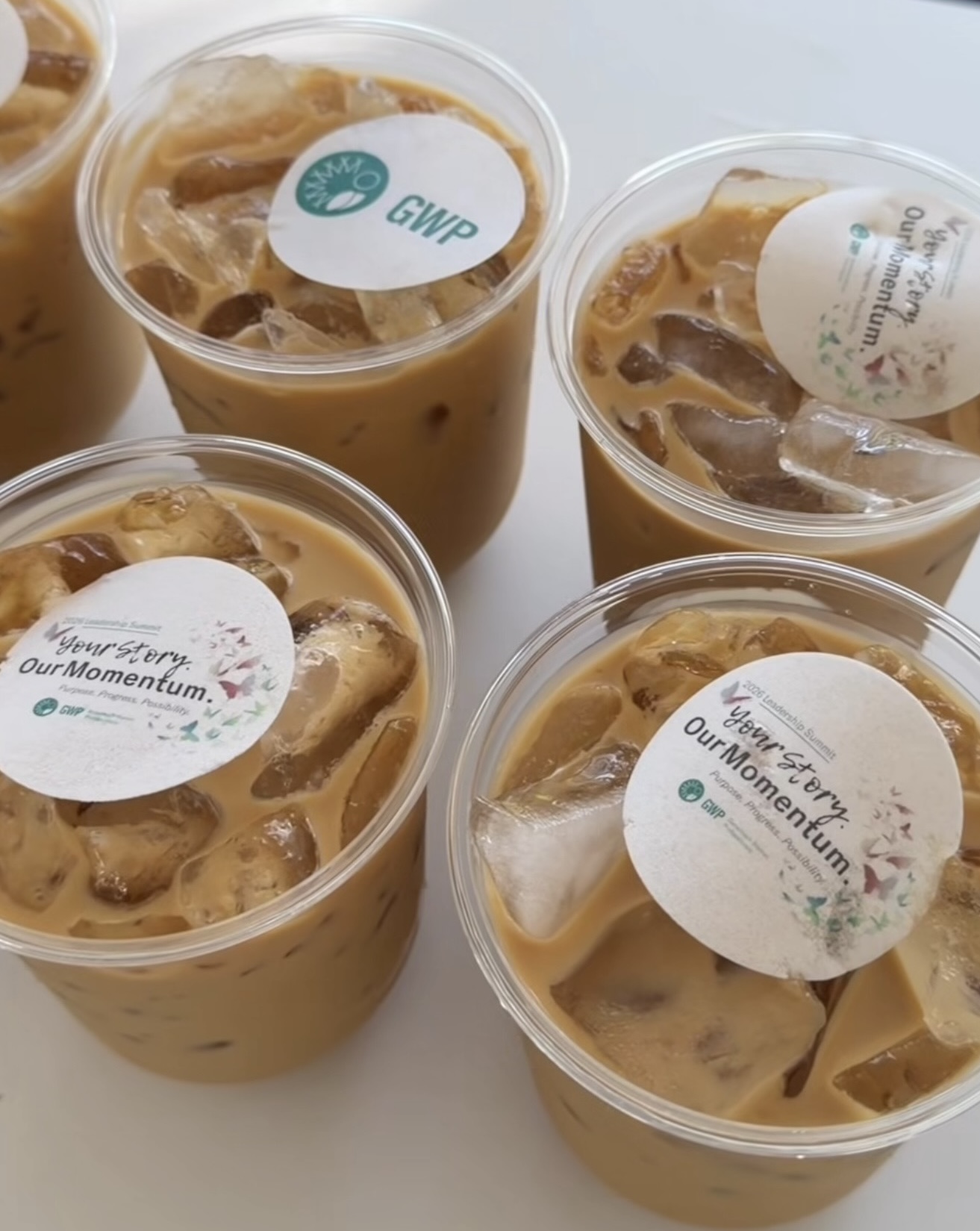 Five plastic cups filled with iced coffee, each sealed with a sticker on top.