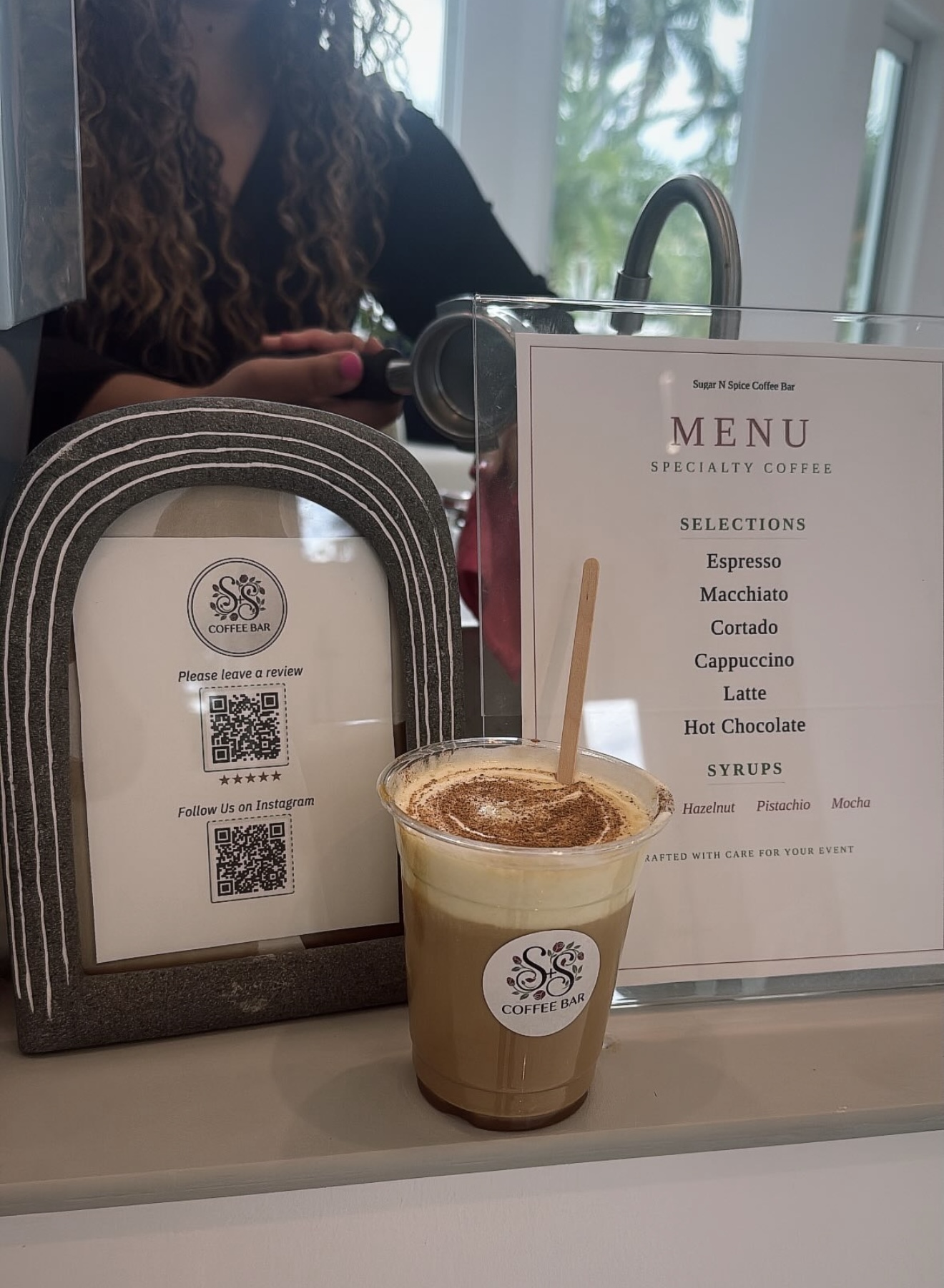 Coffee cup with froth and cinnamon next to menu and a sign with QR codes at coffee bar counter.