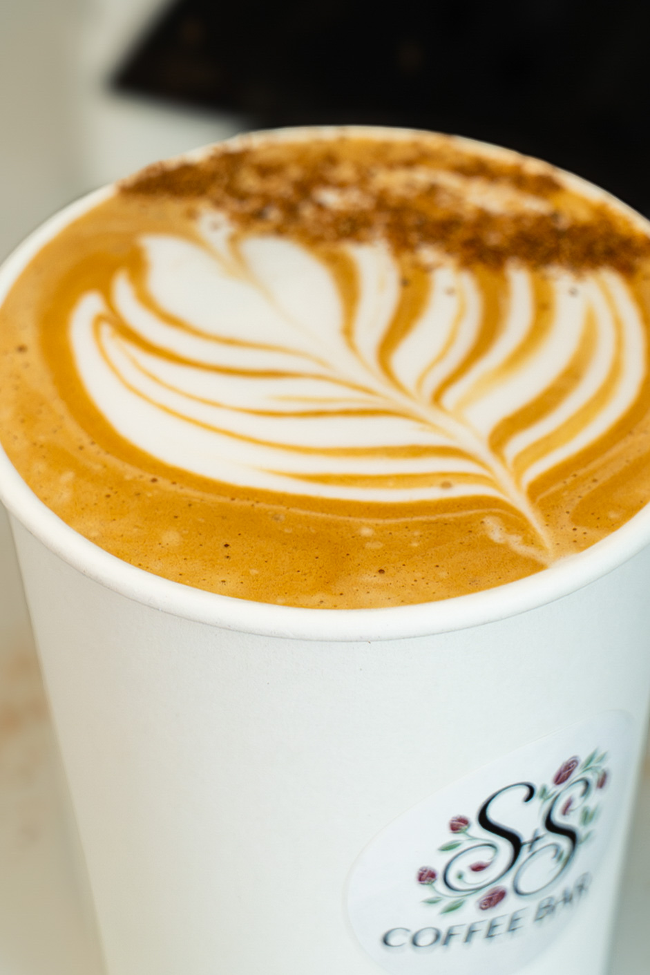 White coffee cup with latte art leaf design and brown sprinkles on top from SS Coffee Bar.