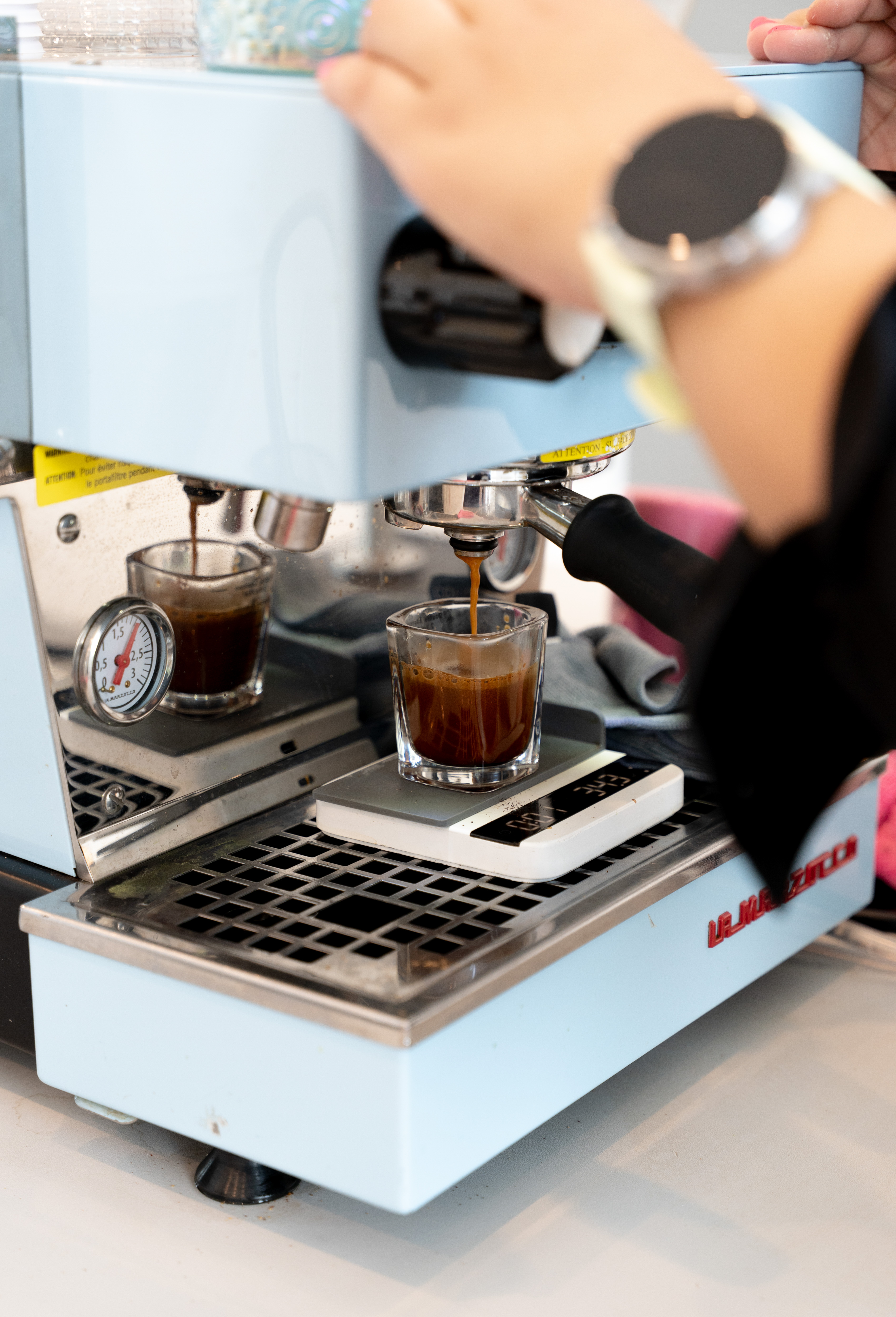 Close-up of coffee machine brewing espresso into a glass with a barista's hand adjusting it.