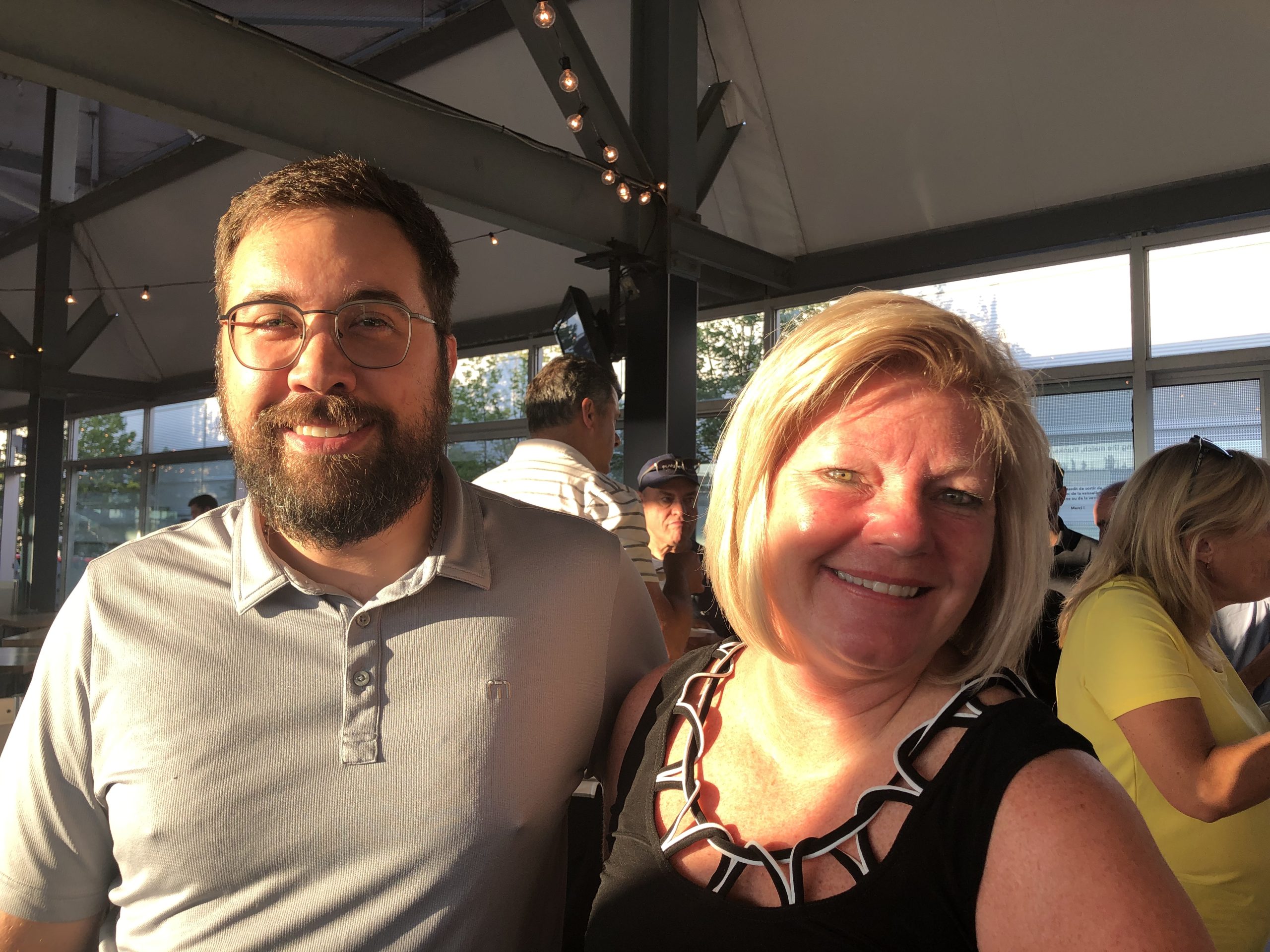 Two people smiling in a bright indoor space with string lights