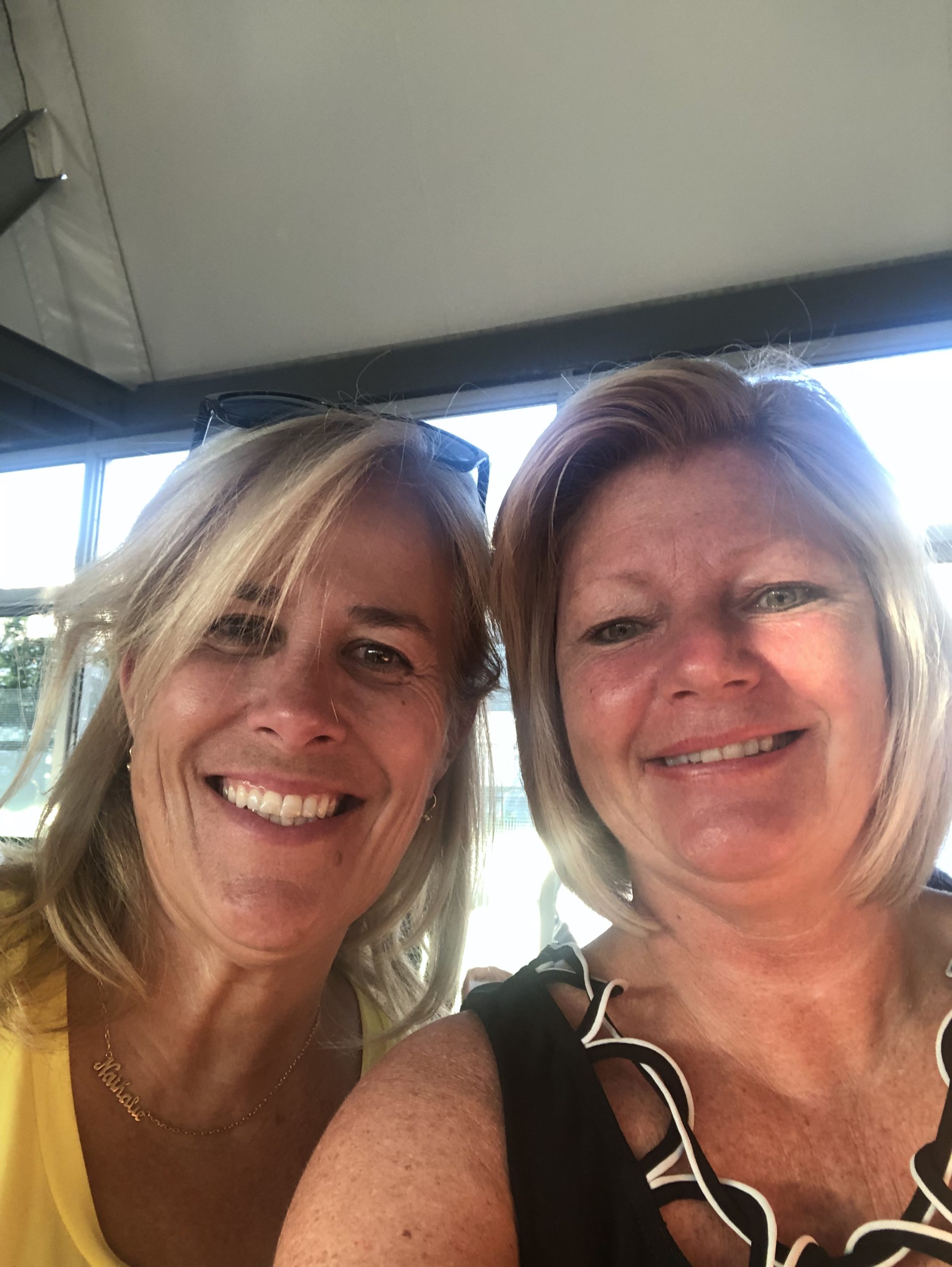 Two middle-aged women smiling together near a window