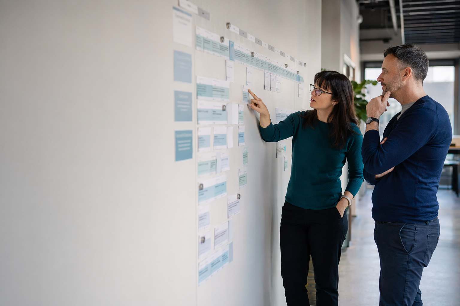 Chef de projet et collègue passant en revue un long échéancier d'implantation ERP affiché sur un mur de fiches de phases dans un bureau québécois.