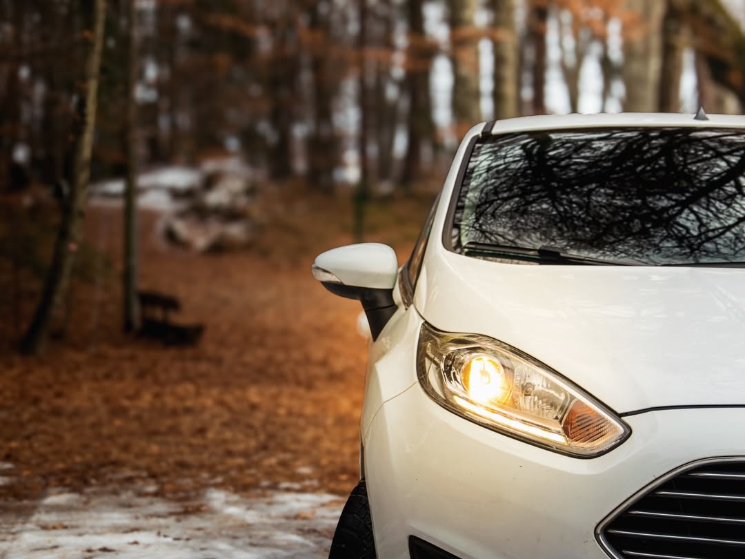 Weißes Auto mit Scheinwerfer im herbstlichen Wald mit fallenden Blättern