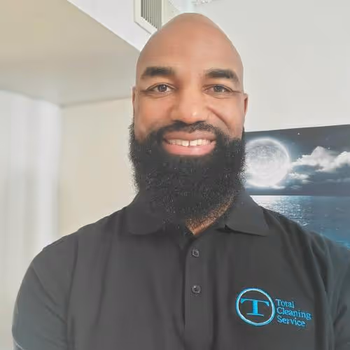 Smiling bald man with a full beard wearing a black polo shirt with a Total Cleaning Service logo.