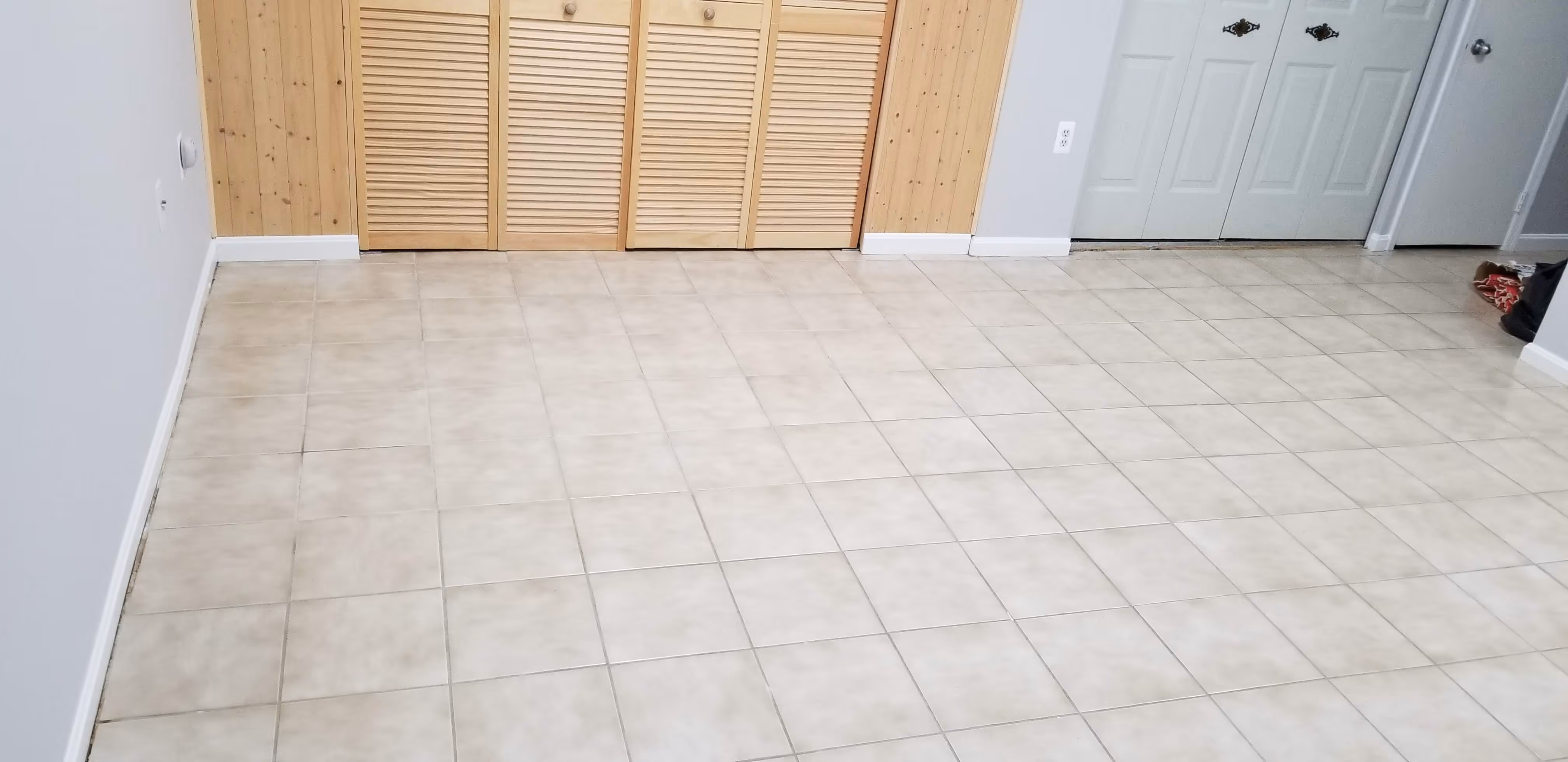 Room with light beige tiled floor, white walls, wooden closet doors, and a white entry door with decorative handles.