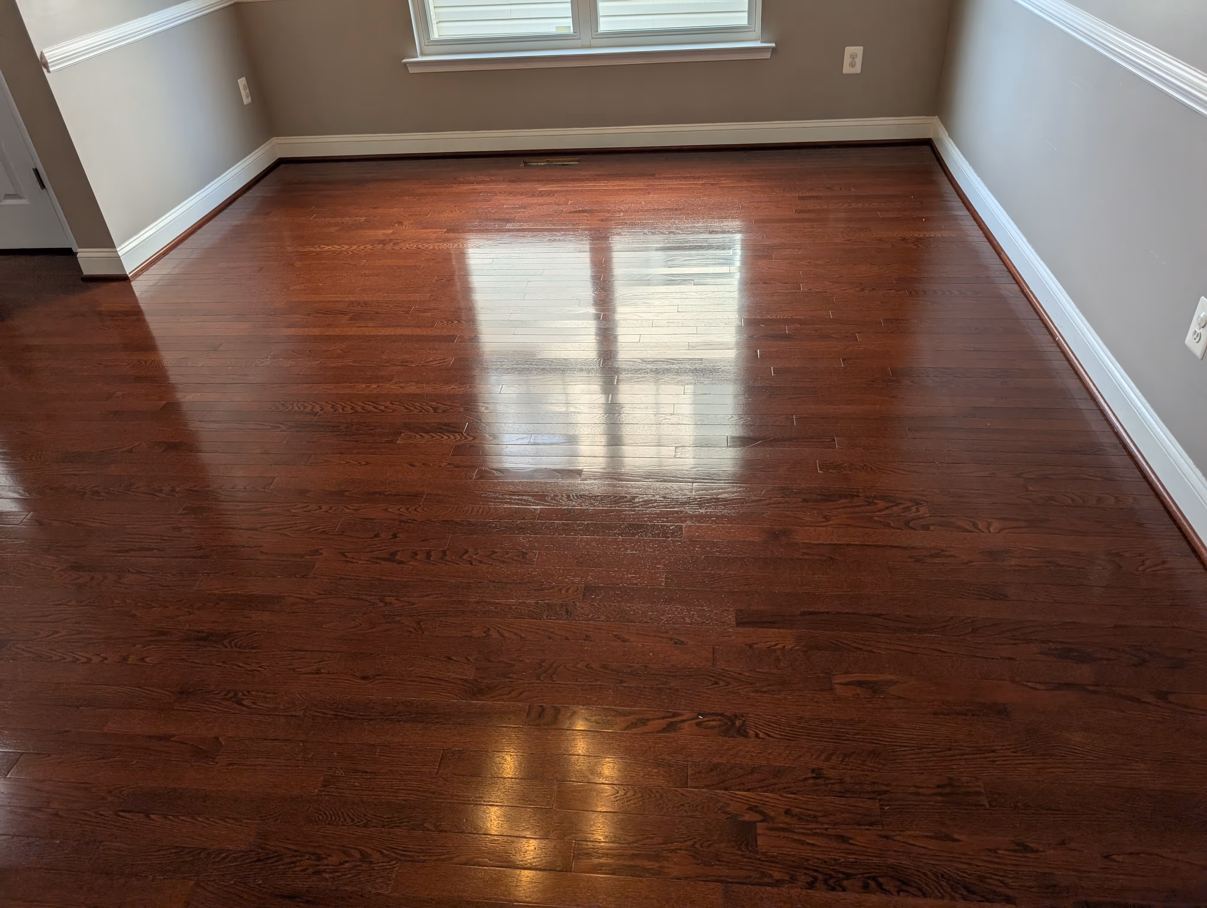 Empty room with polished dark hardwood flooring and beige walls under a window.