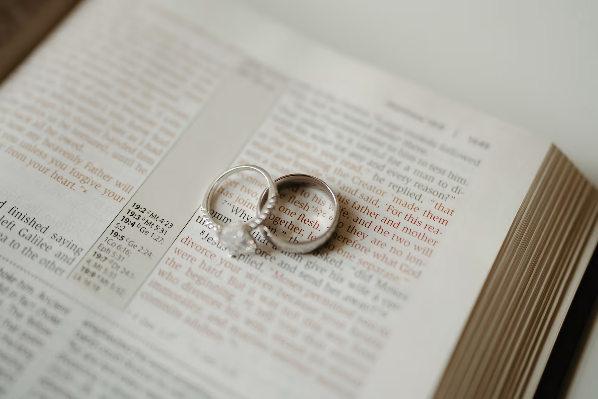 Wedding and engagement rings casting heart-shaped shadows on an open Bible page.