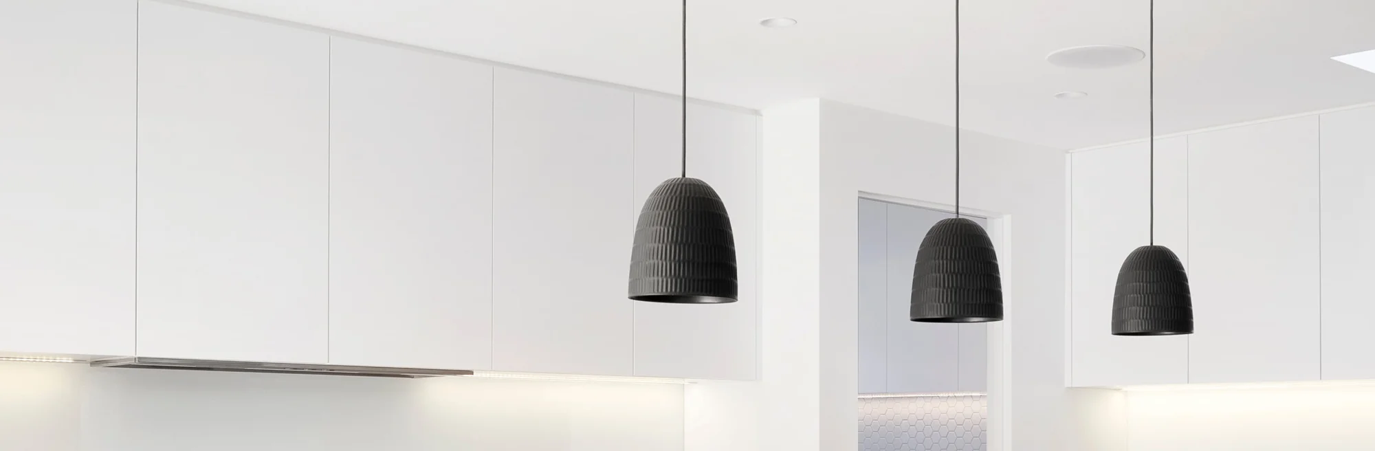 Modern white kitchen cabinets with black pendant lights.
