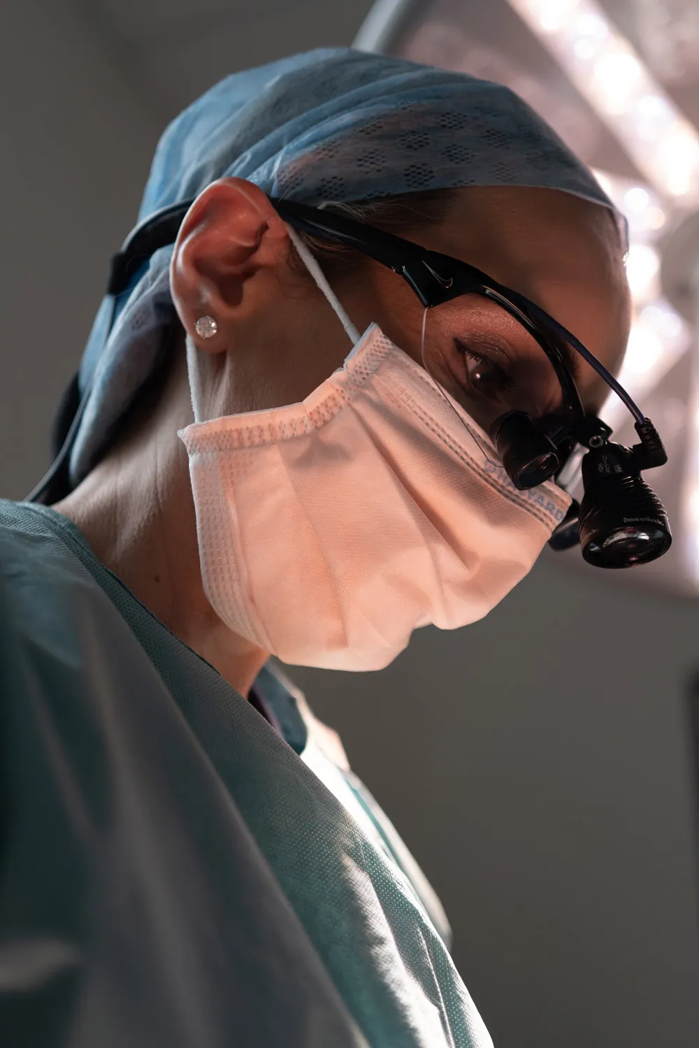 Close-up of a female surgeon wearing a surgical mask, cap, and magnifying glasses during operation.