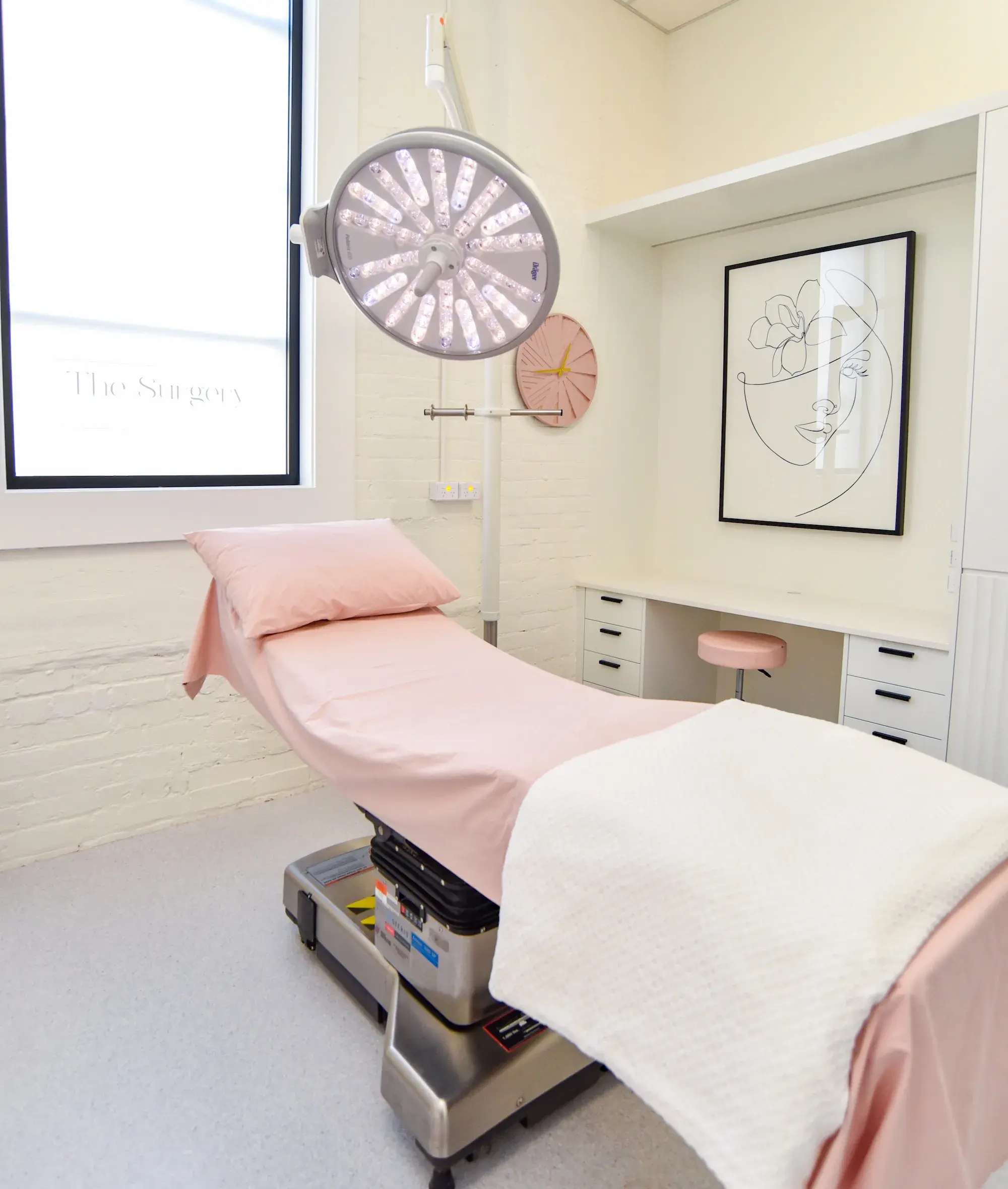 Medical examination room with pink-covered bed, overhead surgical light, and modern decor.