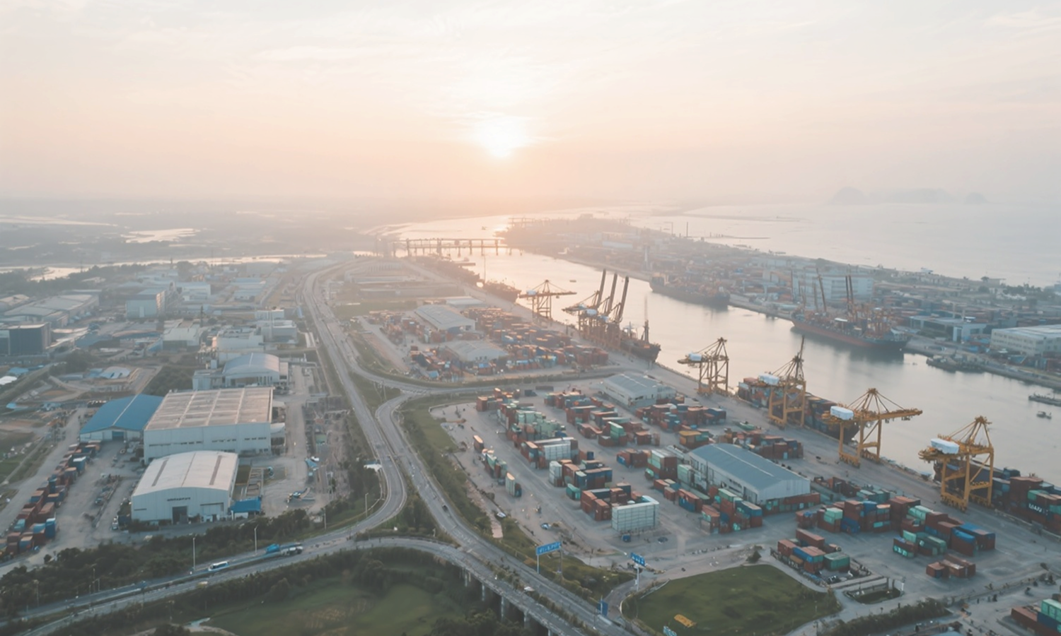Aerial view of a large shipping port with containers, cranes, and ships during sunset.