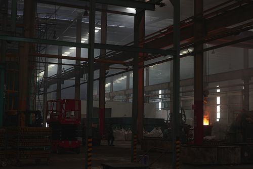 Dimly lit industrial warehouse with machinery, metal structures, and a bright fire or molten material glowing on the right side.