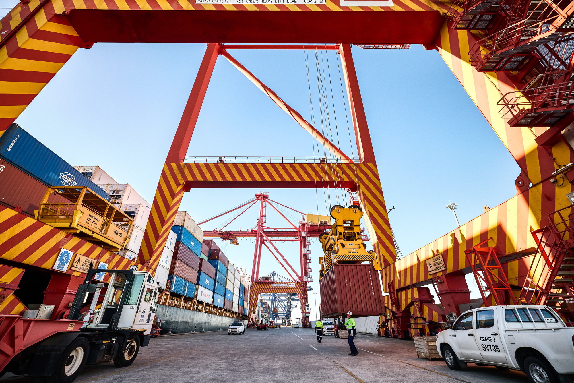 Workers and machinery operating at a busy shipping port, with large cranes moving shipping containers.