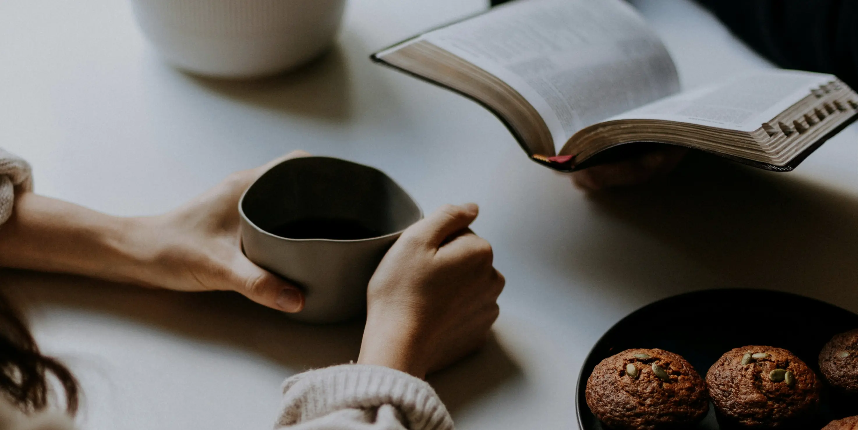 A person sitting at a table with a book and a cup of coffee.