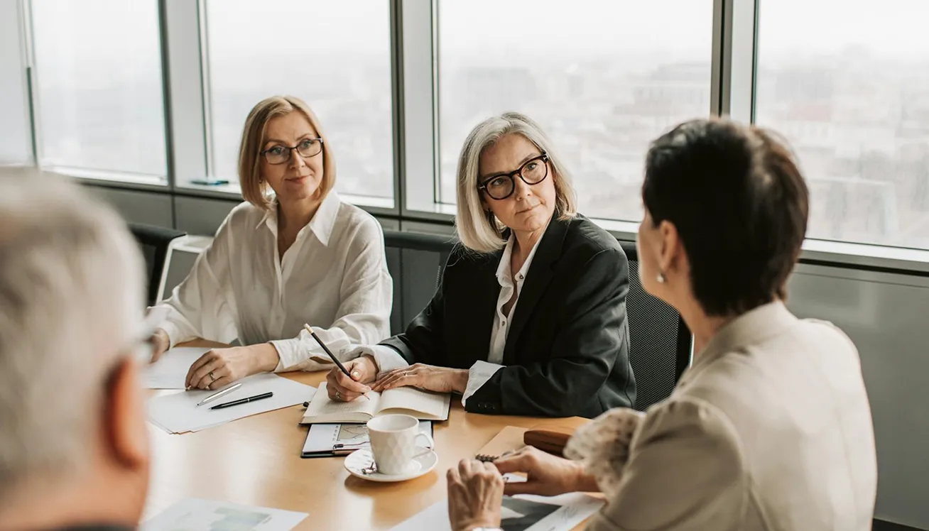Four business professionals having a meeting around a conference table in a modern office with large windows.
