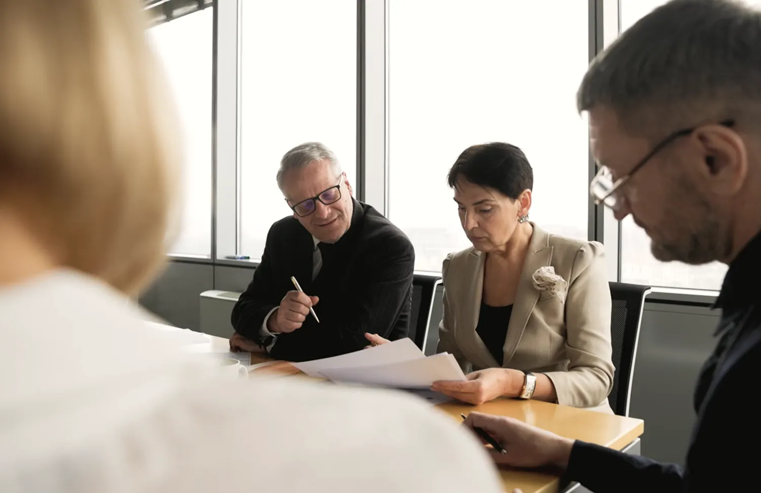 Three professionals sitting at a conference table reviewing documents in a modern office with large windows.