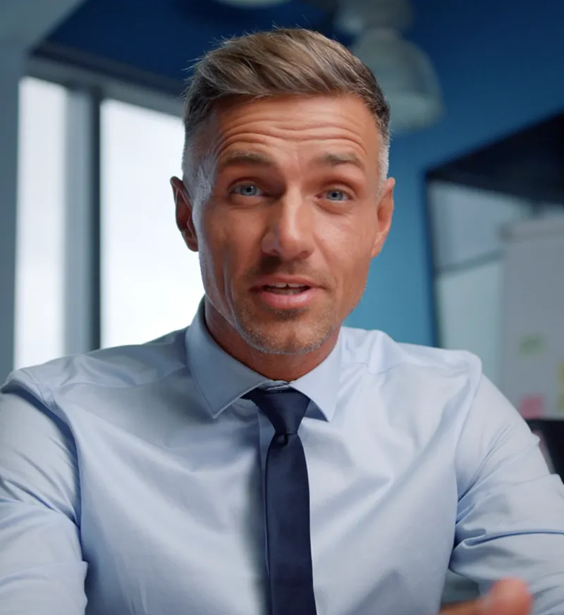 Middle-aged man with blue eyes and short hair wearing a light blue shirt and dark tie speaking indoors.