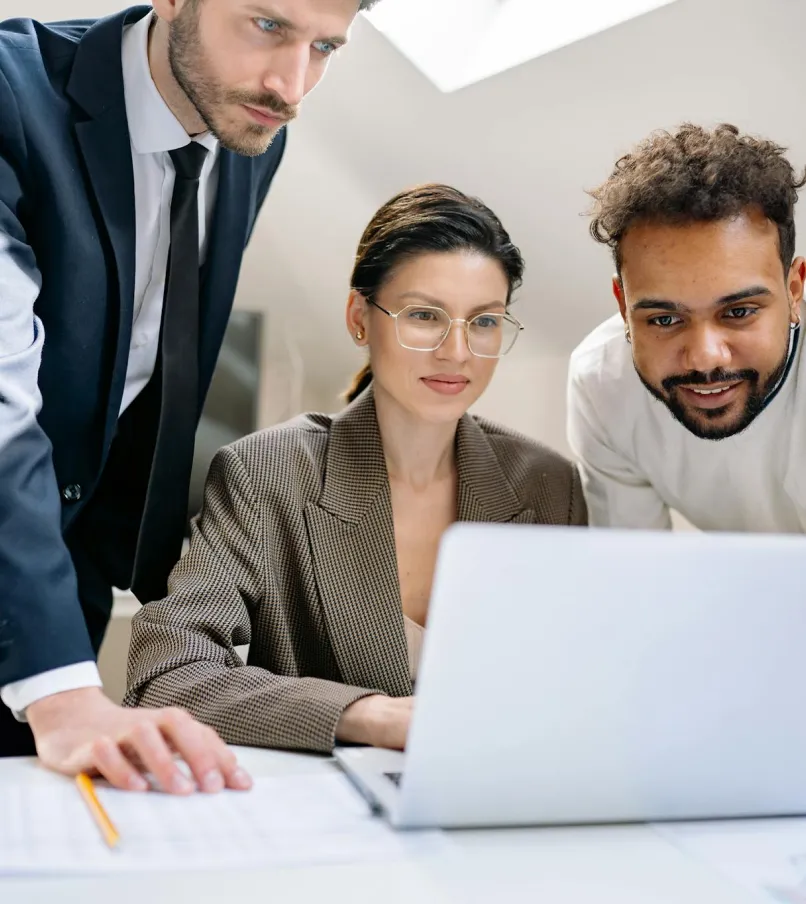 Three diverse business colleagues focused on a laptop screen during a meeting in a modern office.