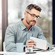 Smiling man with glasses holding a tablet, seated at a desk with a glass of water.