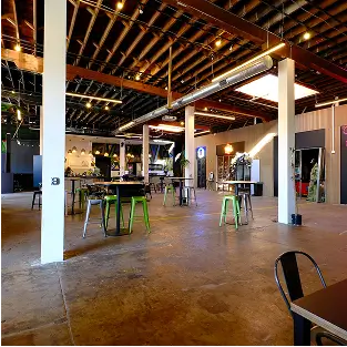 Spacious industrial-style café interior with concrete floors, exposed ceiling beams, and tables with stools scattered around.