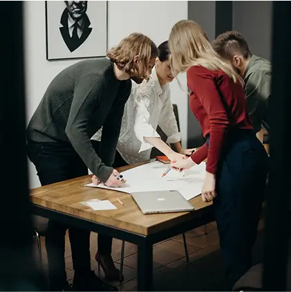 Four people collaborating around a wooden table with a laptop and papers, discussing work.