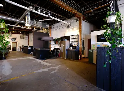 Open office space with industrial ceiling, desks, chairs, plants, and storage cabinets.