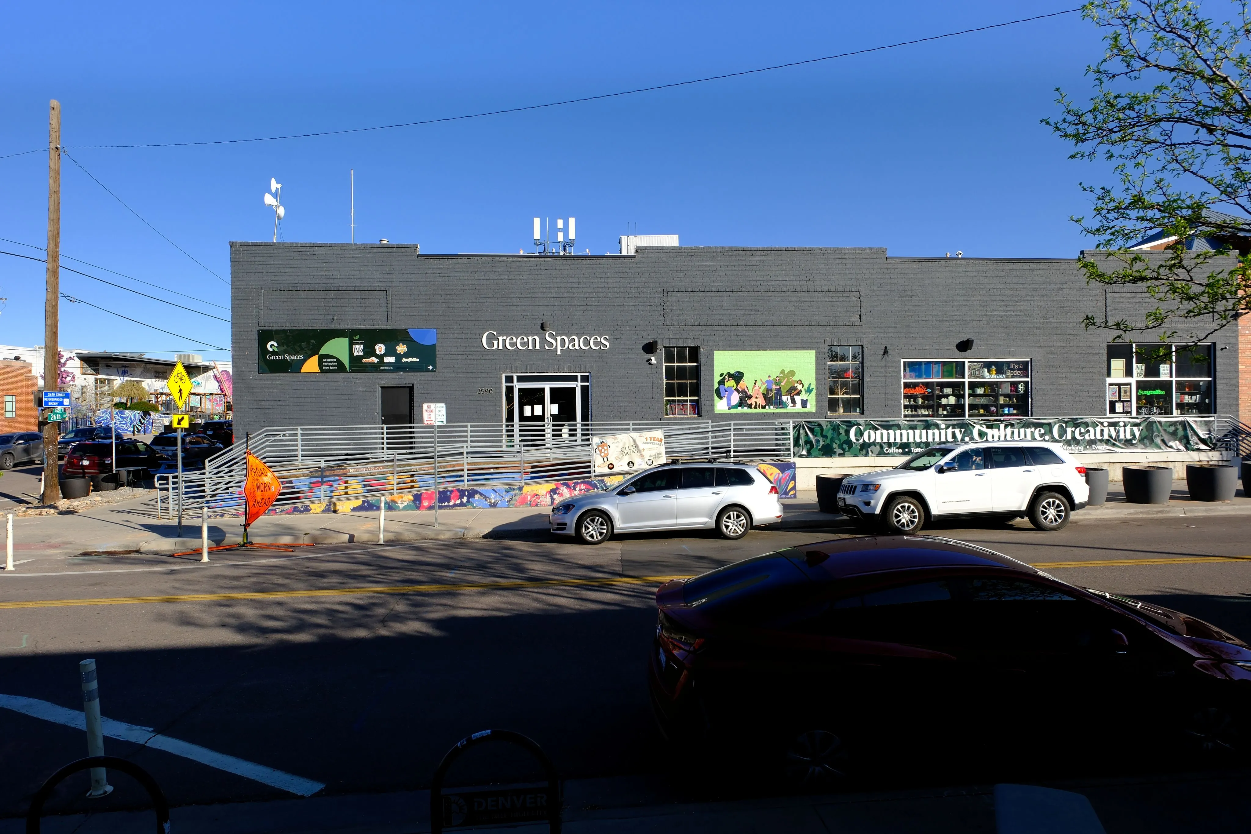 Gray building with 'Green Spaces' sign, colorful mural, and parked cars under a clear blue sky.