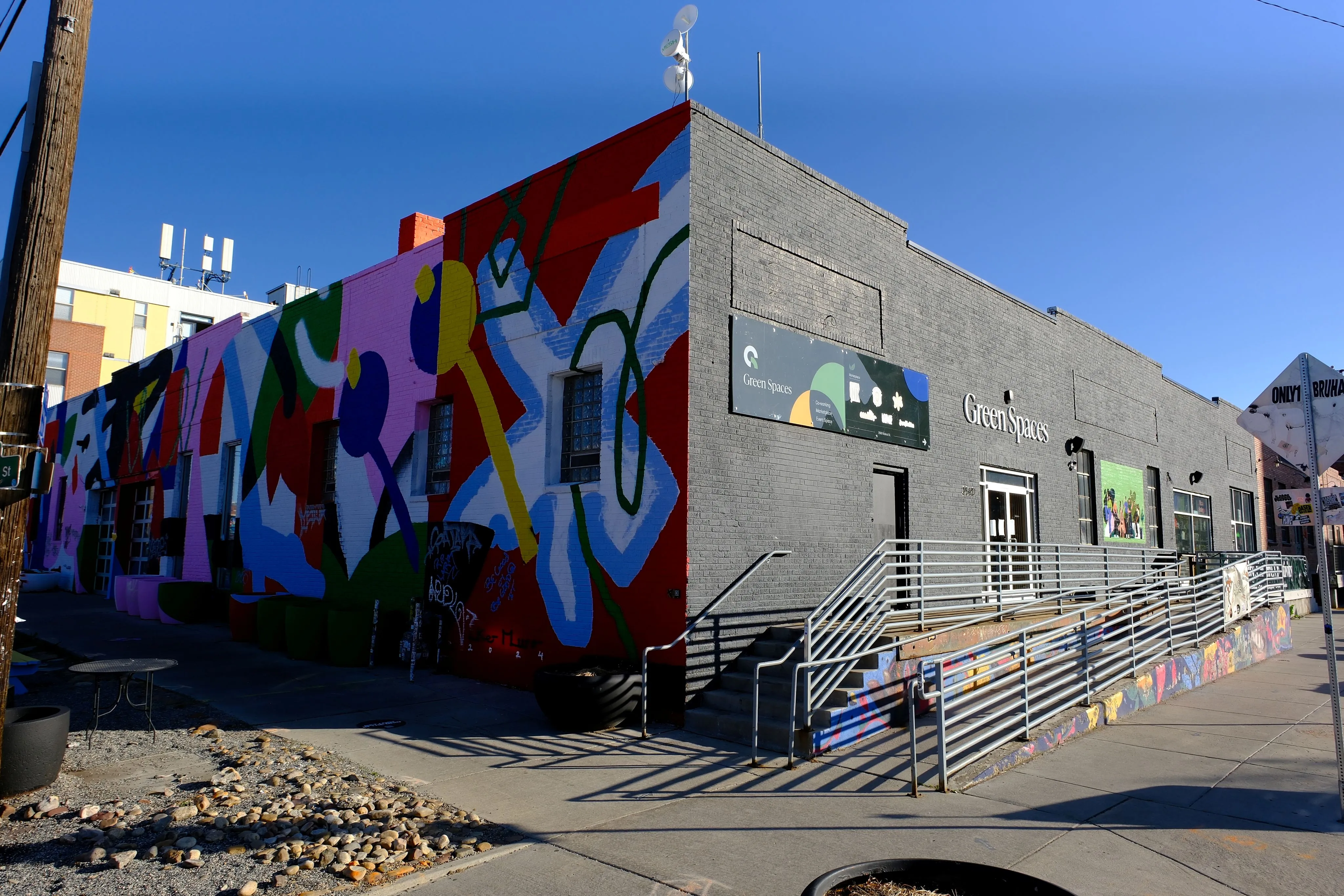 Corner building with 'Green Spaces' sign, gray brick facade, and one side covered in colorful abstract mural art.