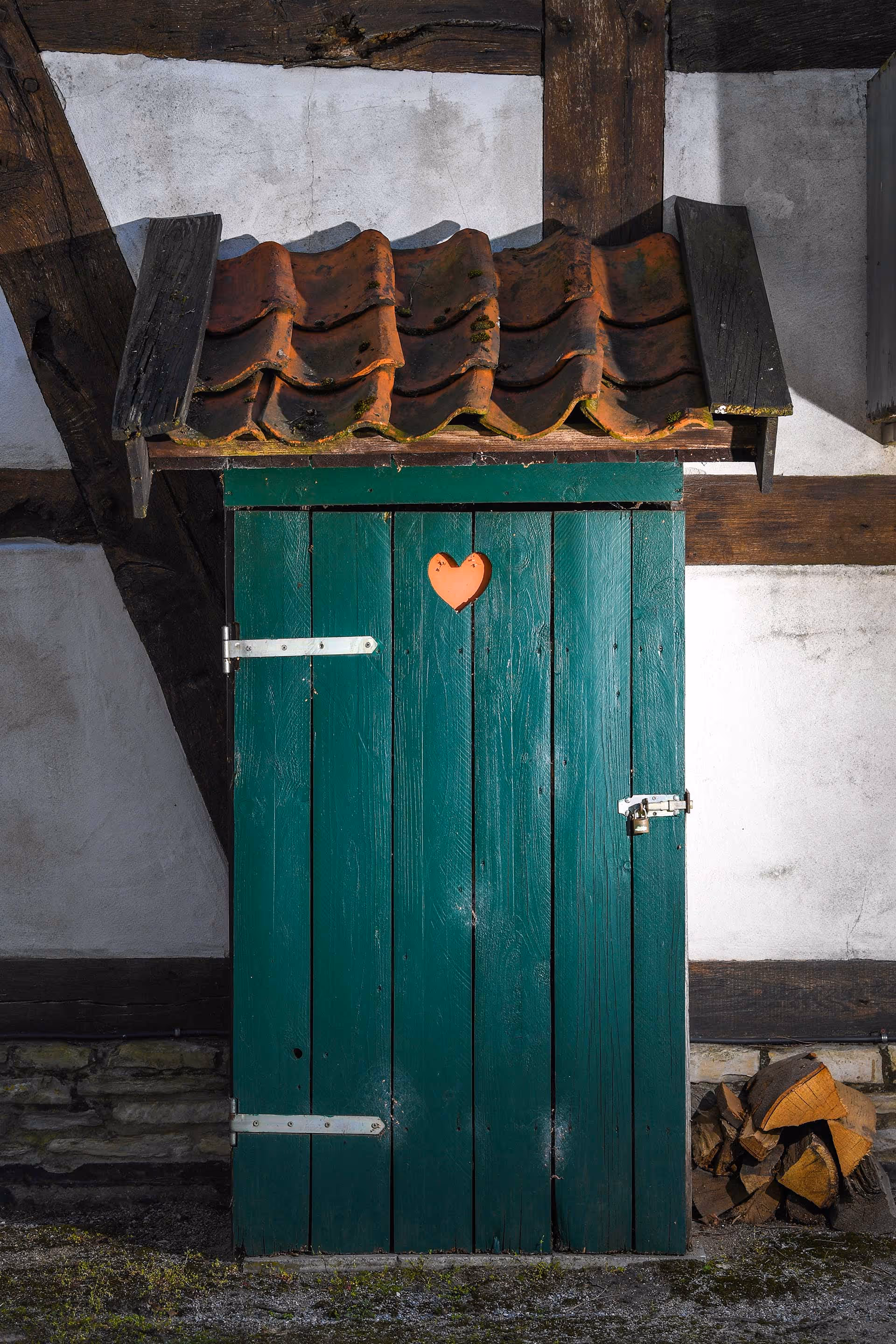 Eine grüne Holztür mit einem kleinen roten Herz mittig dekoriert.