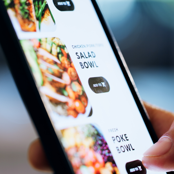 Main tenant un smartphone montrant une application de commande en ligne avec des options de salade bowl et poke bowl.
