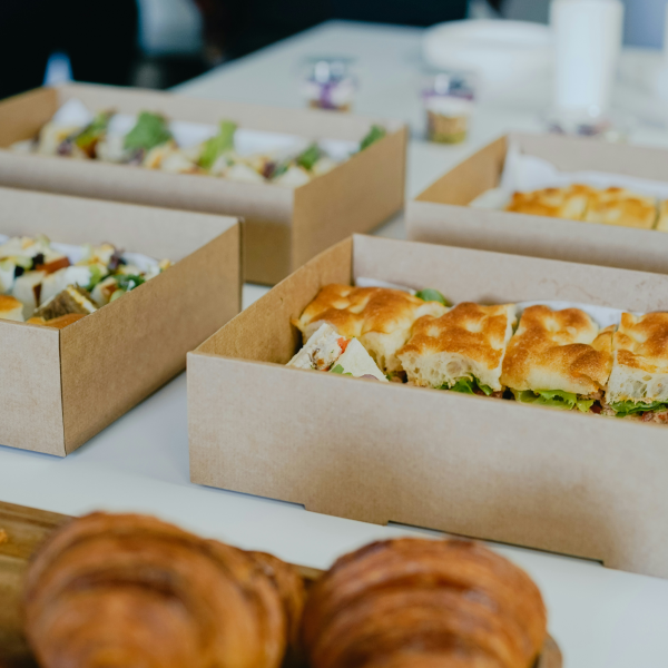 Boîtes en carton contenant des sandwichs et des salades, avec des croissants flous au premier plan.