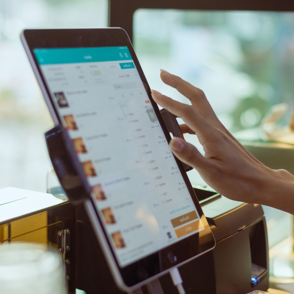 Une main humaine utilise une tablette tactile affichant un menu numérique dans un environnement de restaurant ou de café.