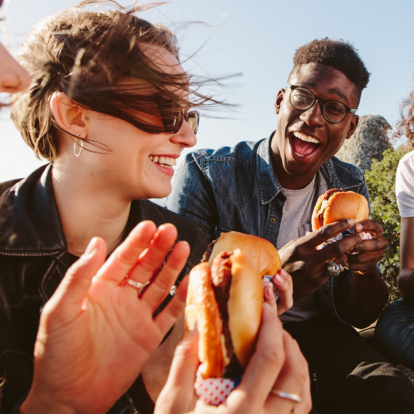 Groupe d'amis souriants mangeant des hamburgers en plein air par une journée ensoleillée.