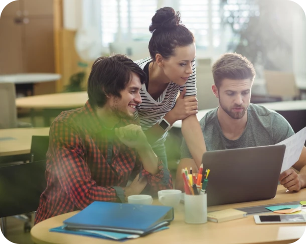 Three young professionals collaborating around a laptop in a modern office setting.