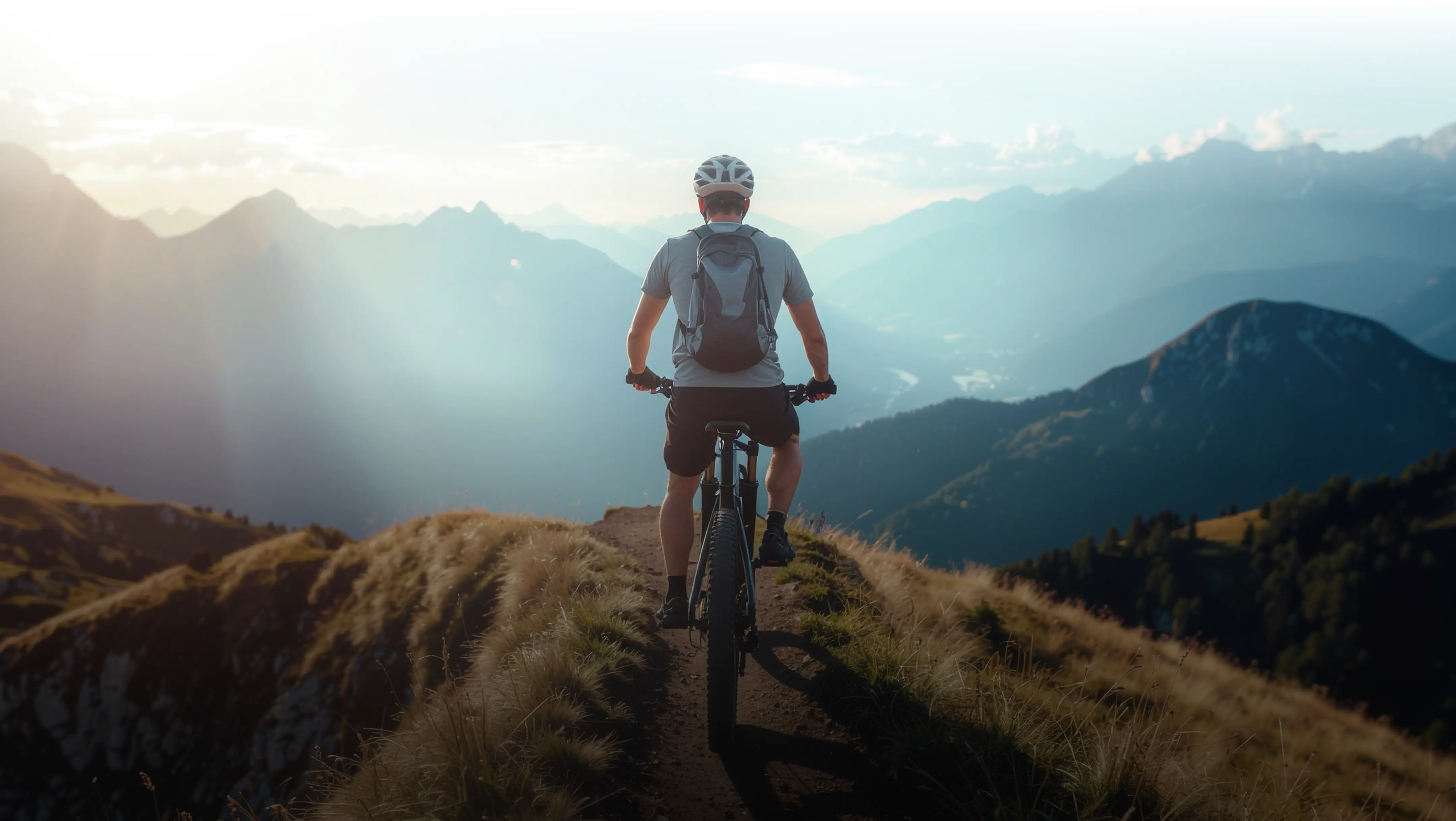 Radfahrer mit Helm und Rucksack fährt auf einem schmalen Bergpfad mit Blick auf neblige Berge.