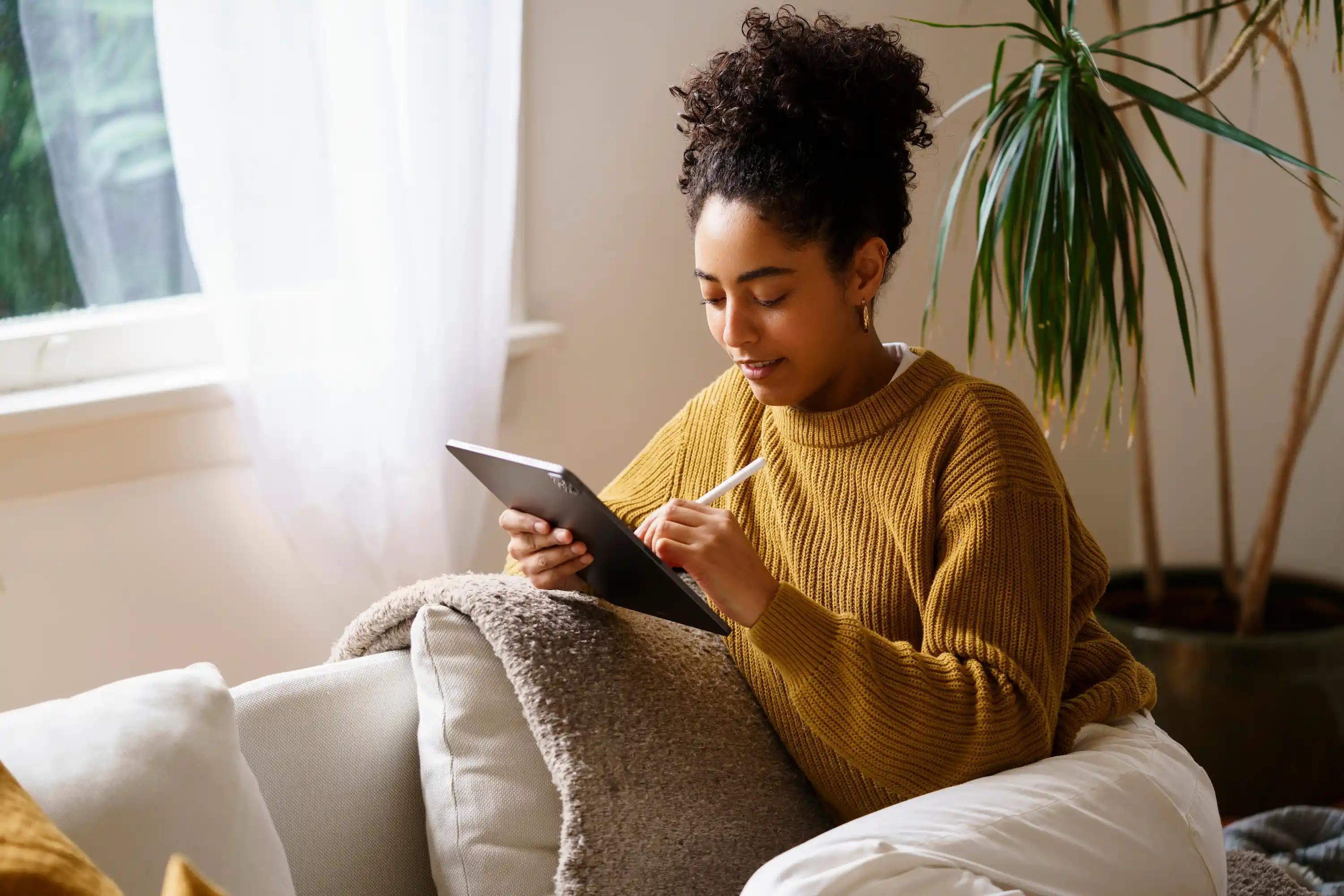 Frau sitzt gemütlich auf dem Sofa und benutzt ein Tablet mit einem Eingabestift.