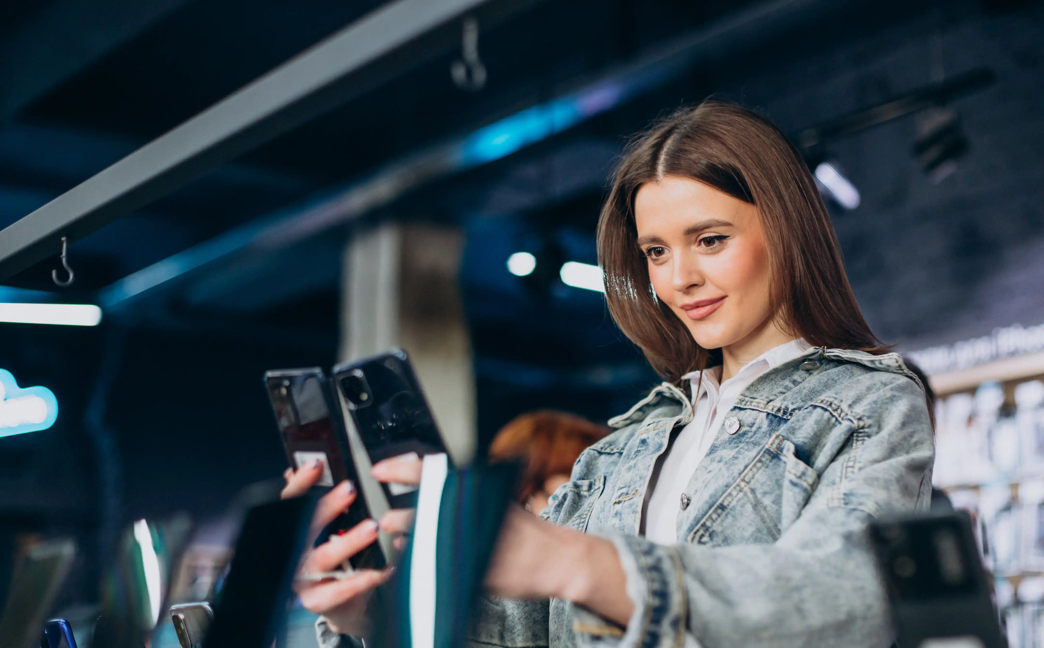 Frau mit Jeansjacke, die in einem Elektronikgeschäft zwei Smartphones vergleicht.