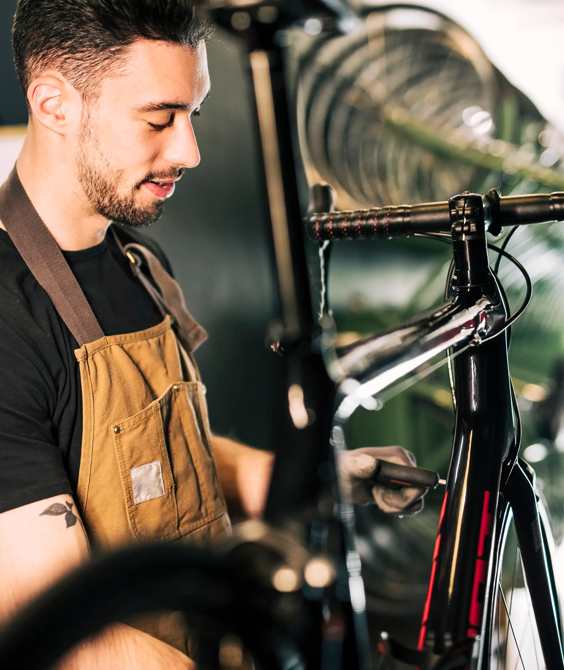 Ein Mann in brauner Schürze repariert mit einem Werkzeug ein schwarzes Rennrad.