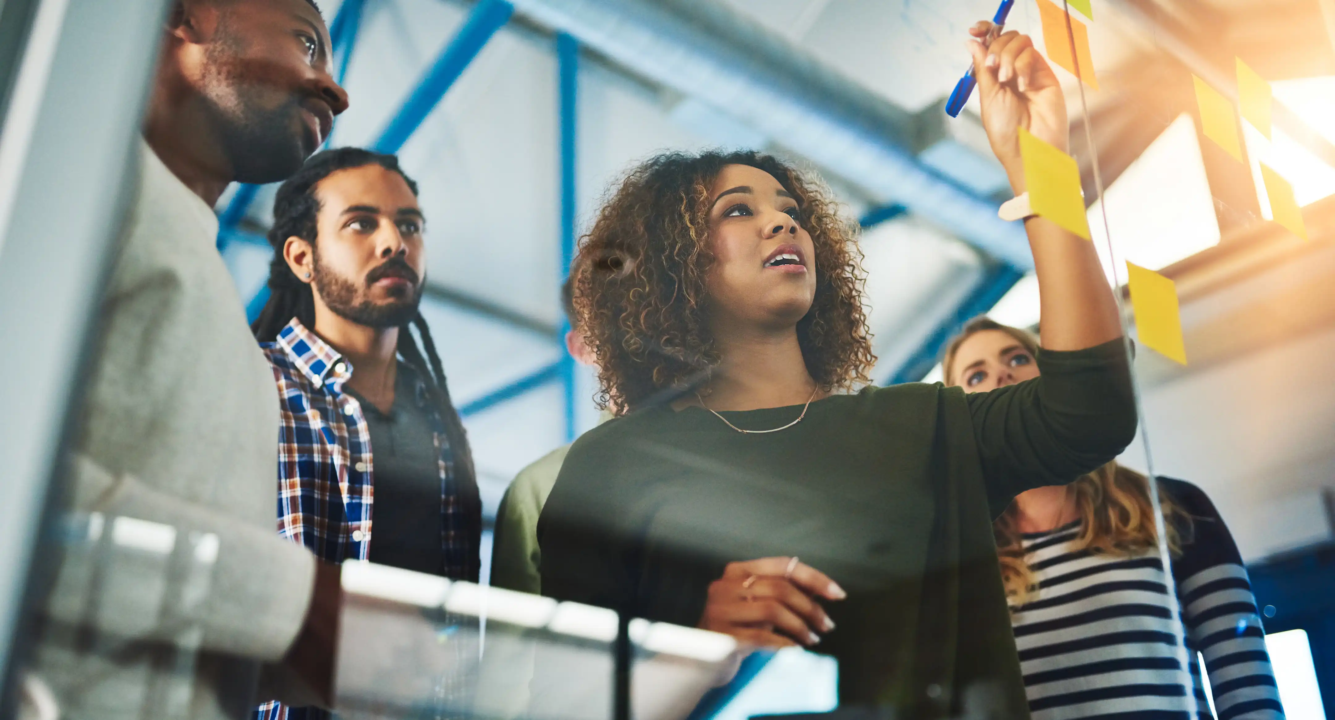 Gruppe von vier Personen diskutiert und notiert Ideen auf gelben Haftnotizen an einer Glaswand in einem modernen Büro.
