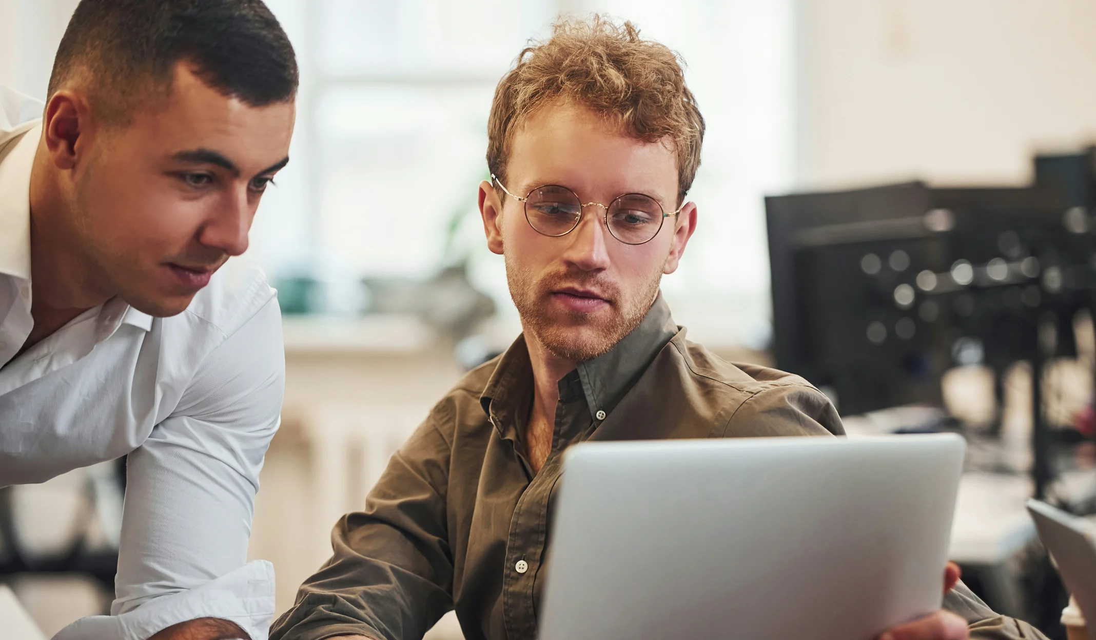 Zwei junge Männer betrachten gemeinsam einen Laptop in einem modernen Büro.
